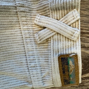 May include: Close-up of a beige and white striped fabric with a brown label that says "Mountain Hardwear" and a mountain graphic. The fabric is folded over and tied in a knot.