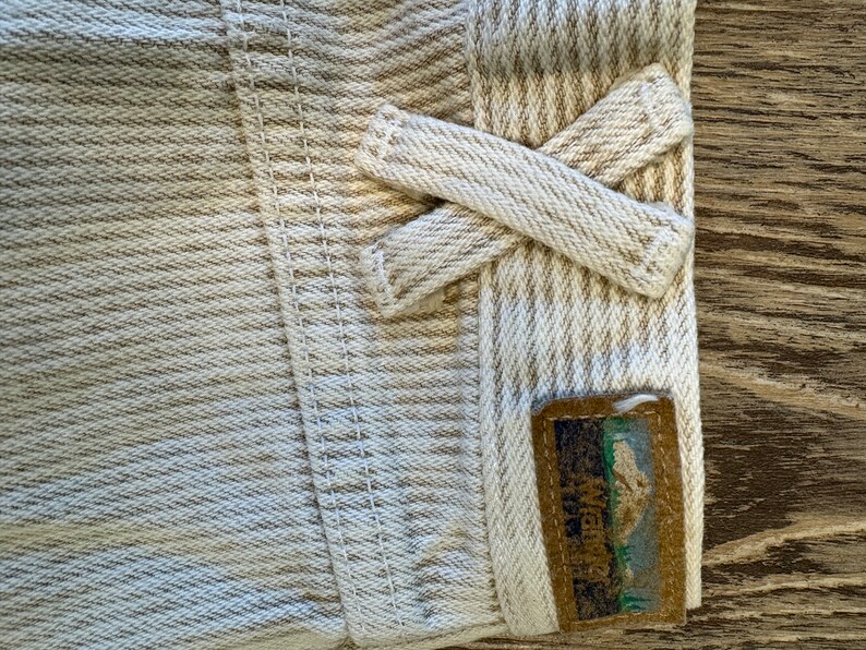 May include: Close-up of a beige and white striped fabric with a brown label that says "Mountain Hardwear" and a mountain graphic. The fabric is folded over and tied in a knot.