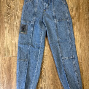 K&ouml;nnte beinhalten: Hellblaue Jeanshose mit elastischem Bund und mehreren Taschen. Die Hose hat einen Aufn&auml;her mit der Aufschrift "Wrangler Outdoor Adventure". Die Hose hat eine lockere Passform und ist an den Kn&ouml;cheln ger&uuml;scht.