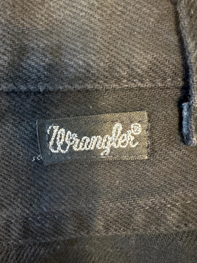K&ouml;nnte beinhalten: Ein schwarzes Wrangler-Markenetikett mit wei&szlig;en N&auml;hten.
