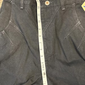 May include: Dark gray denim pants with a high waist and decorative stitching. A measuring tape shows a length of approximately 14 inches. The pants have a button closure and belt loops.