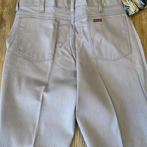 May include: Light blue Wrangler jeans with a classic five-pocket design. The jeans have a straight leg cut and a small red Wrangler logo patch on the back pocket. A blue and white tag is attached.