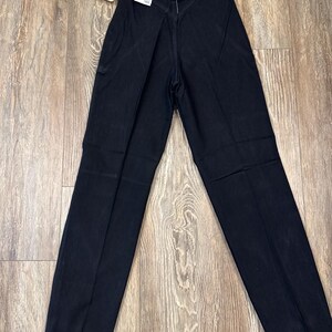 May include: Black Wrangler jeans with a straight leg design. The jeans have a classic five-pocket style and a high waist. A tag is attached to the jeans.