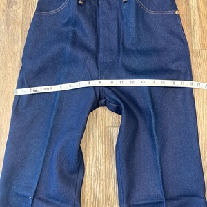 May include: Dark blue denim jeans with a straight leg design. The jeans have classic five-pocket styling, a button and zipper closure, and a measuring tape across the waist. The waist measures approximately 10 inches across.