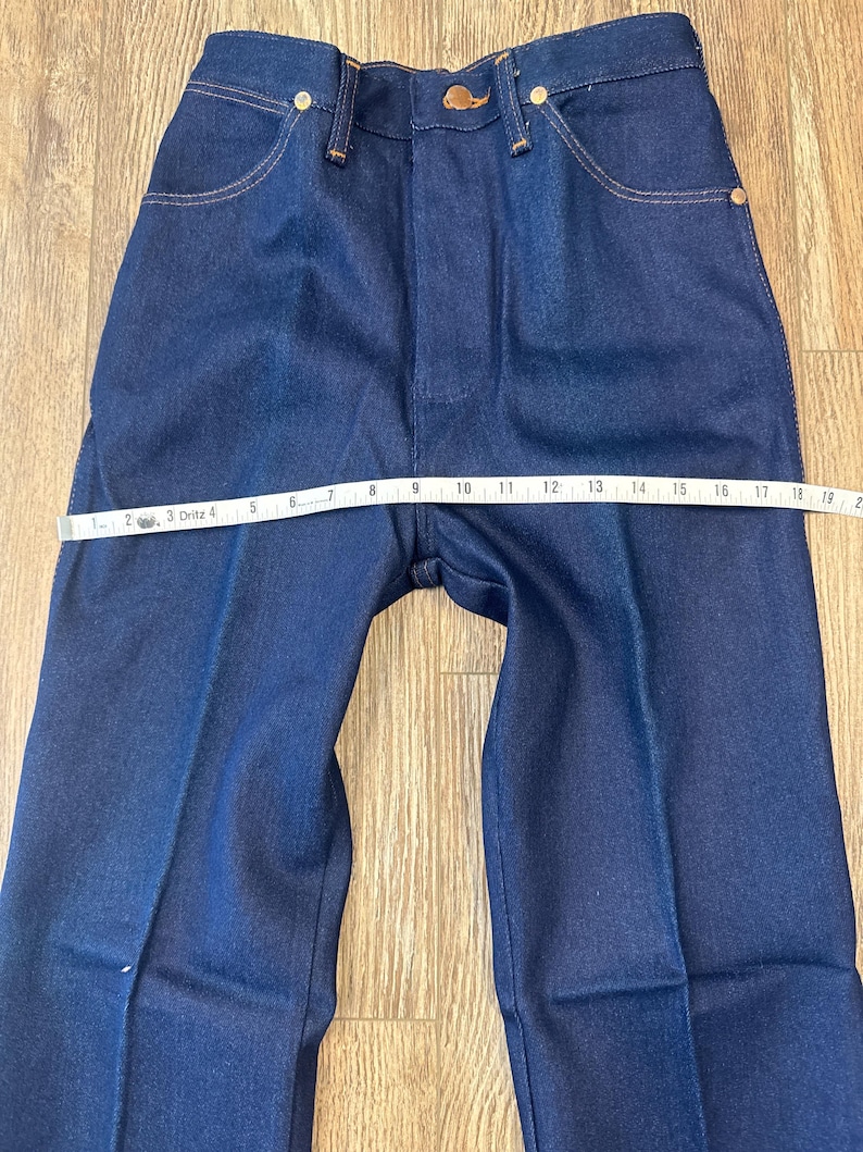 May include: Dark blue denim jeans with a straight leg design. The jeans have classic five-pocket styling, a button and zipper closure, and a measuring tape across the waist. The waist measures approximately 10 inches across.