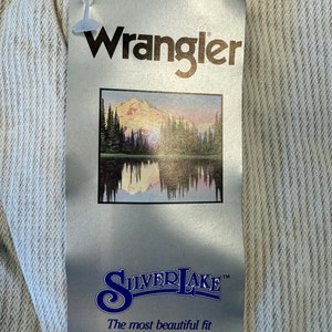 May include: A white Wrangler Silverlake jeans tag with a mountain scene and the text "The most beautiful fit in the West."
