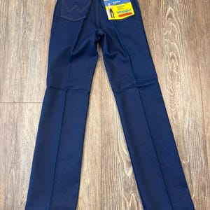 May include: Dark blue Wrangler jeans with a high waist and straight leg. The jeans have a classic five-pocket design and a Wrangler label on the back pocket. The jeans are new with tags.