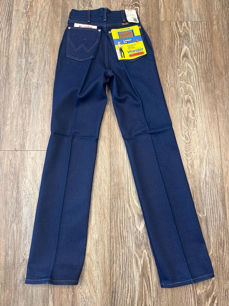May include: Dark blue Wrangler jeans with a high waist and straight leg. The jeans have a classic five-pocket design and a Wrangler label on the back pocket. The jeans are new with tags.