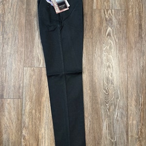 Op de afbeelding: Zwarte jeans met een Wrangler Silverlake Original Fit-label eraan bevestigd. De jeans is dubbelgevouwen en ligt plat op een houten vloer.