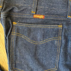 May include: A pair of dark blue denim jeans with a back pocket and a Wrangler label.