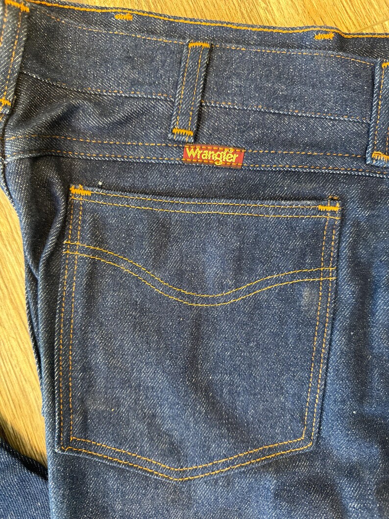 May include: A pair of dark blue denim jeans with a back pocket and a Wrangler label.