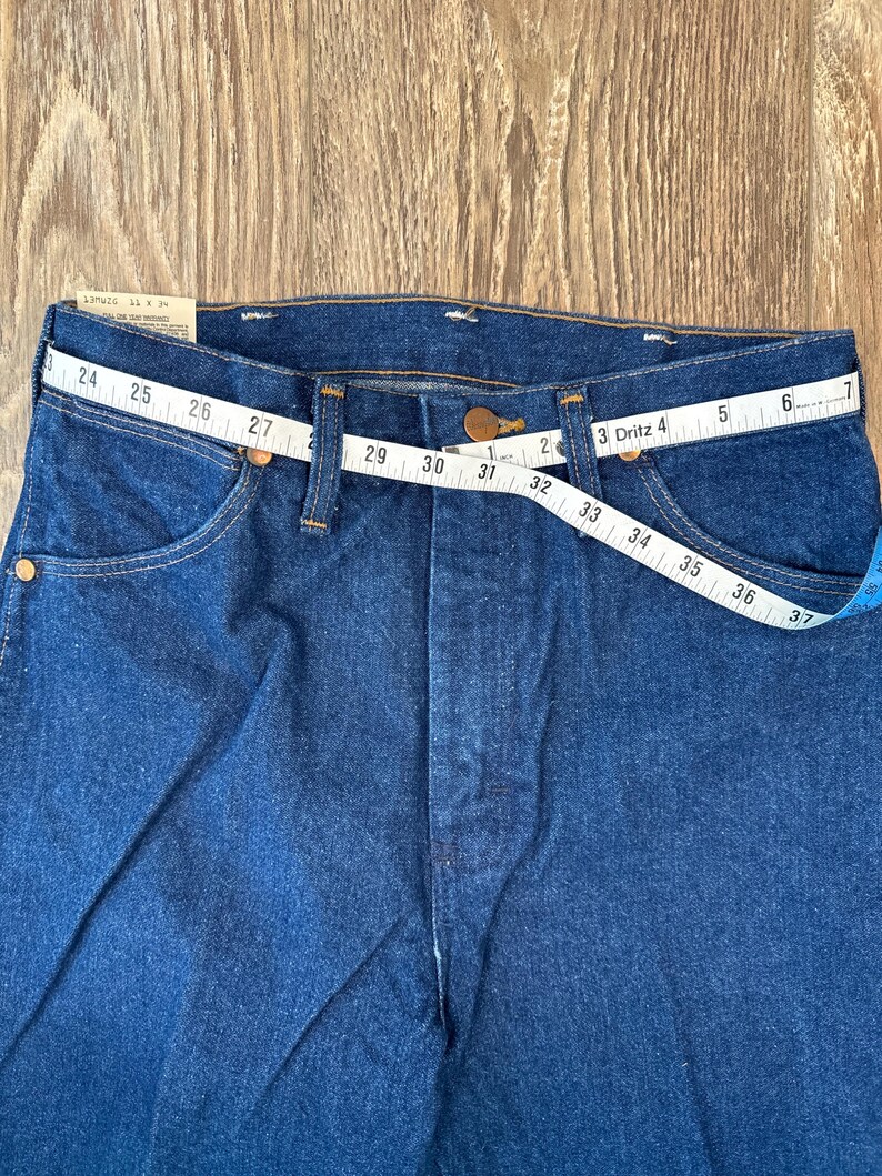 May include: A pair of blue denim jeans with a measuring tape wrapped around the waistband. The tape reads 24 to 37 inches.
