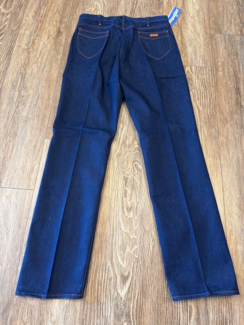 May include: A pair of dark blue denim jeans with a Wrangler tag. The jeans have a straight leg and a classic fit.