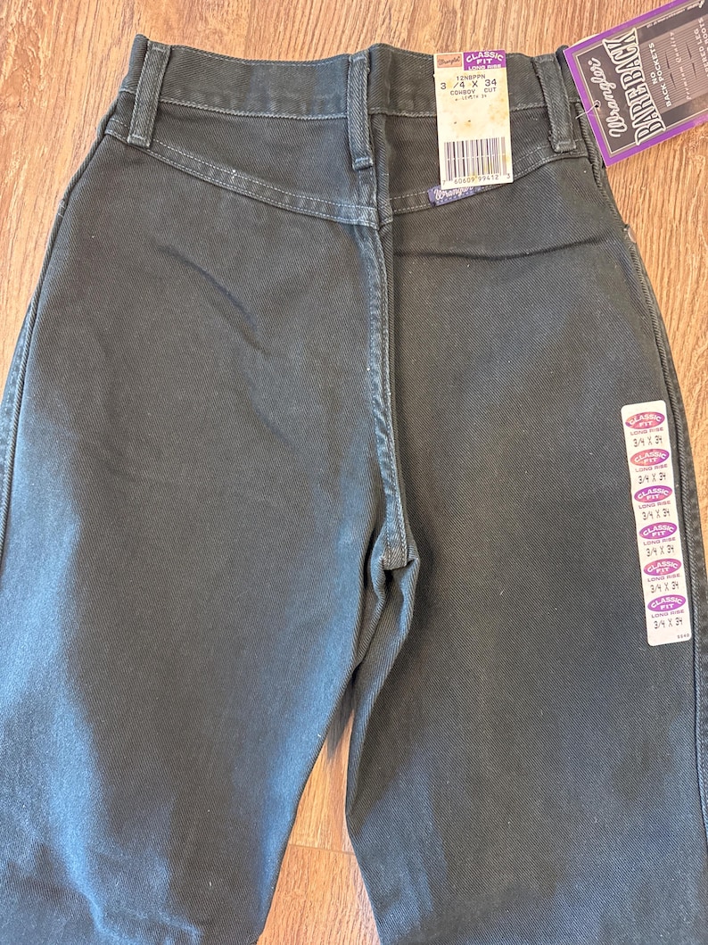 May include: A pair of dark wash Wrangler jeans with a classic fit. The jeans have a size tag that reads "Classic Fit 3/4 x 34 Cowboy Cut".