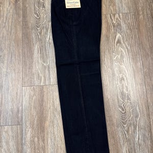 May include: Dark wash Wrangler Silverlake jeans. The jeans are folded and have a tag attached with the Wrangler logo and product information. The jeans are made of a dark blue denim material and are laid out on a light brown wooden surface.