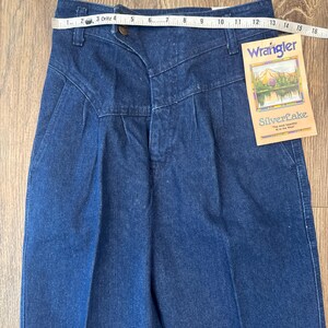Puede incluir: Vaqueros Wrangler Silverlake de mezclilla azul con cintura alta y pliegues. Una cinta m&eacute;trica est&aacute; colocada sobre la cintura. La etiqueta dice "Wrangler SilverLake".