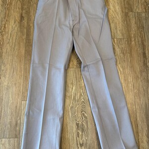 May include: Light gray pants with a button and zipper closure, belt loops, and front and back pockets. The pants are made of a solid-colored fabric and have a straight leg design. A price tag is attached to the pants.