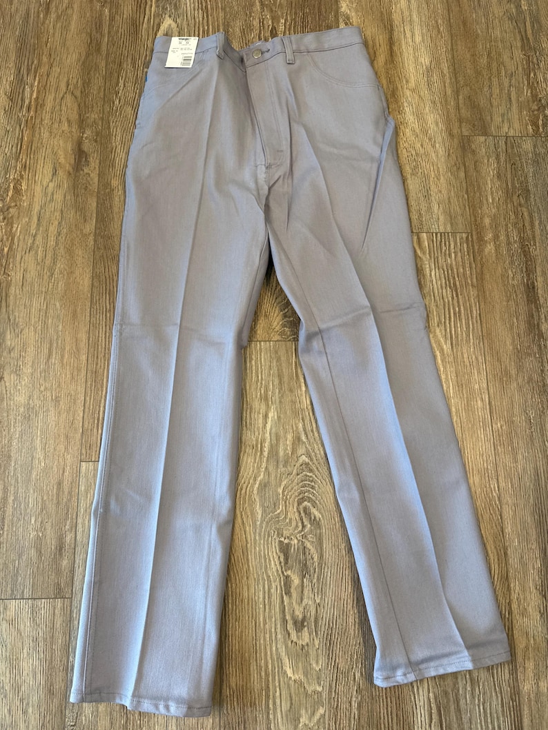 May include: Light gray pants with a button and zipper closure, belt loops, and front and back pockets. The pants are made of a solid-colored fabric and have a straight leg design. A price tag is attached to the pants.