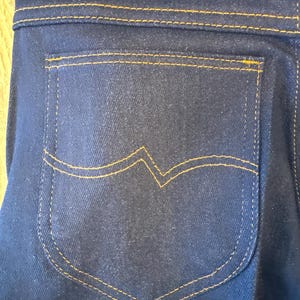 K&ouml;nnte beinhalten: Nahaufnahme einer dunkelblauen Jeans-Ges&auml;&szlig;tasche mit gelber Steppnaht.