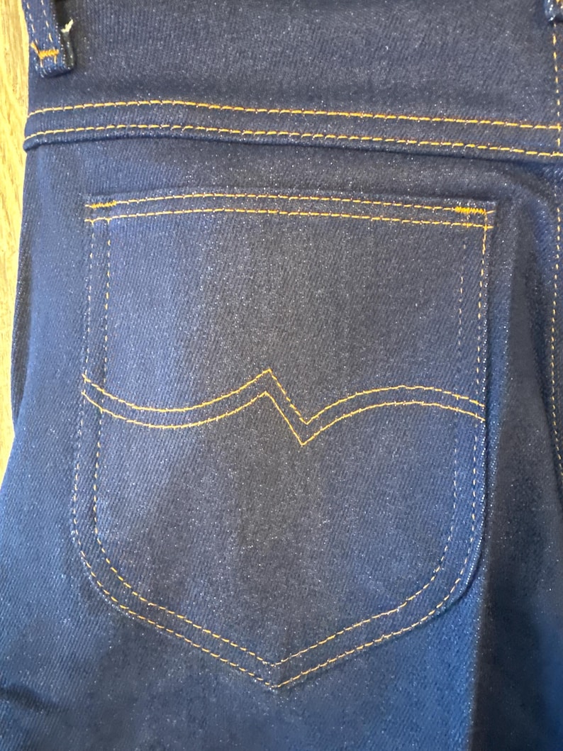 K&ouml;nnte beinhalten: Nahaufnahme einer dunkelblauen Jeans-Ges&auml;&szlig;tasche mit gelber Steppnaht.