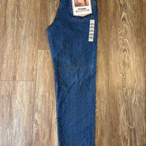 May include: A pair of blue denim jeans with a brown tag that reads "Wrangler Rugged Wear" and "Relaxed Fit".