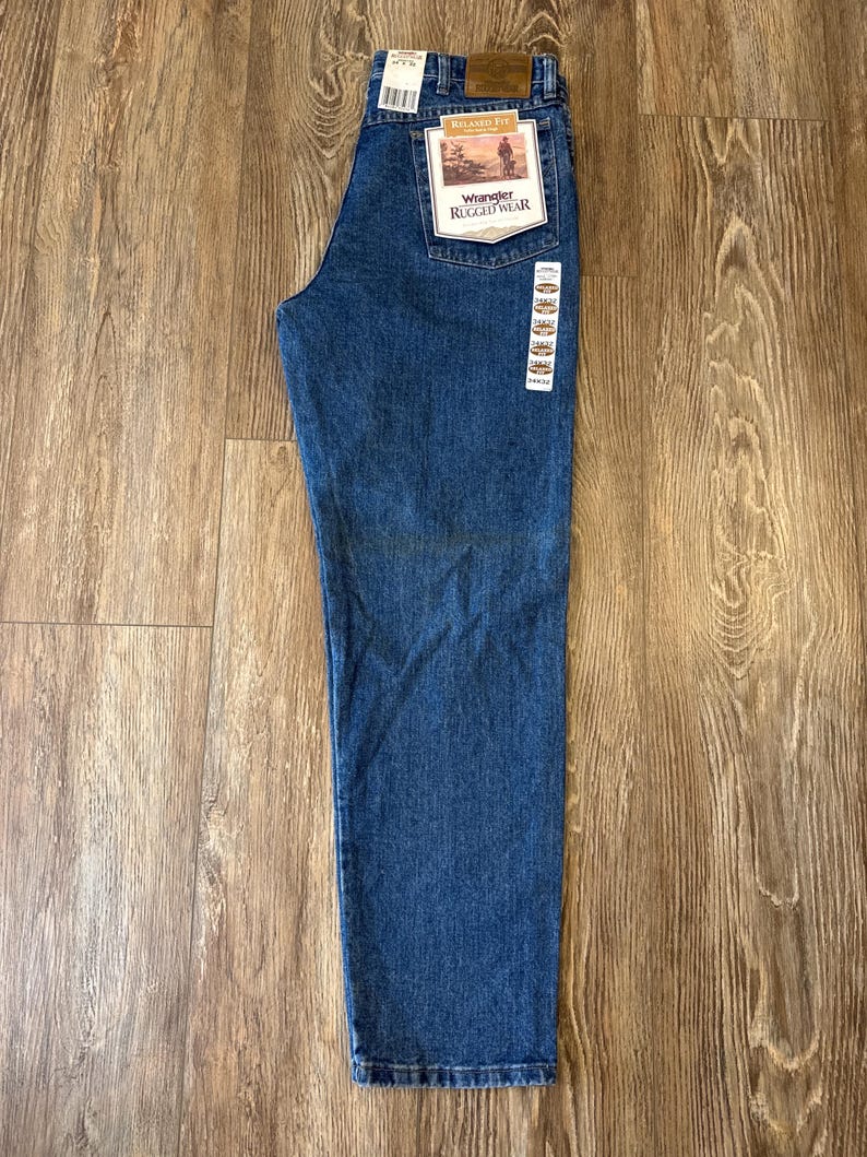 May include: A pair of blue denim jeans with a brown tag that reads "Wrangler Rugged Wear" and "Relaxed Fit".