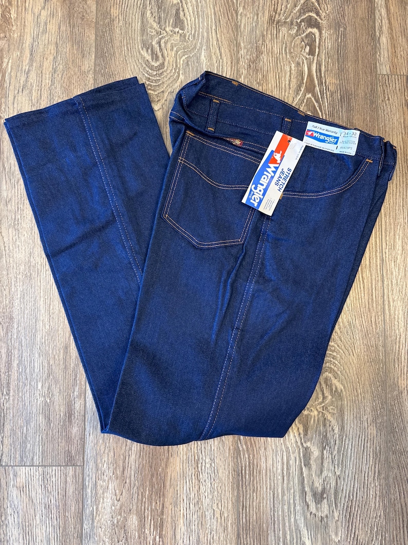 Peut inclure: Un jean en denim bleu fonc&eacute; avec une &eacute;tiquette Wrangler sur la poche arri&egrave;re. L'&eacute;tiquette indique "Stretch Jeans" et "Wrangler".
