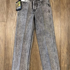 Puede incluir: Vaqueros de mezclilla gris lavados con &aacute;cido con una etiqueta de Wrangler. Los vaqueros tienen un corte recto y un estilo cl&aacute;sico de cinco bolsillos.