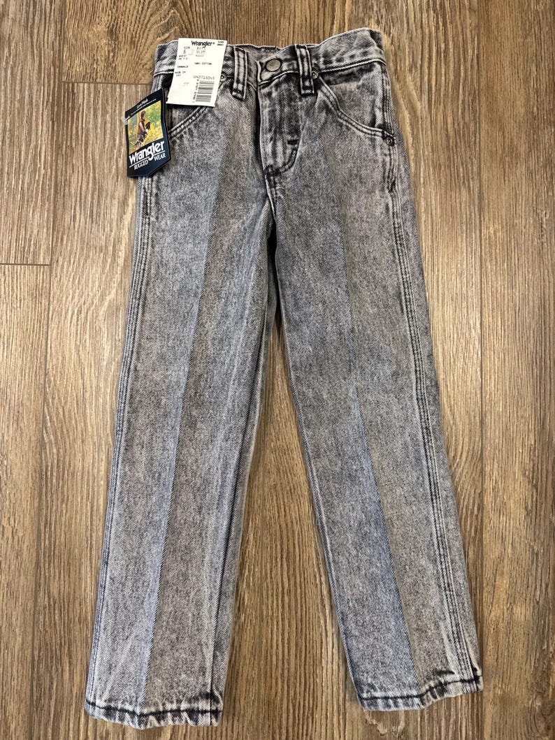 Puede incluir: Vaqueros de mezclilla gris lavados con &aacute;cido con una etiqueta de Wrangler. Los vaqueros tienen un corte recto y un estilo cl&aacute;sico de cinco bolsillos.