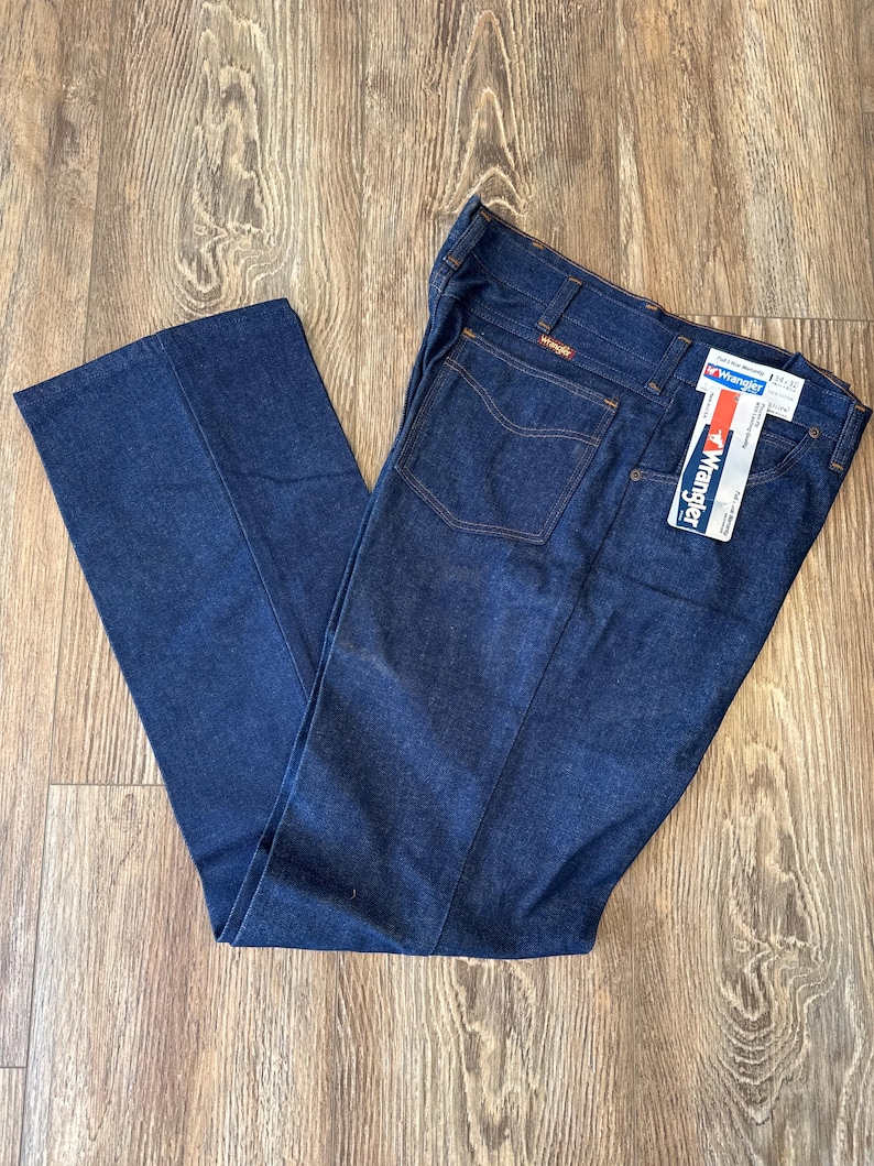 May include: A pair of dark blue denim jeans with a brown leather patch that says "Wrangler" on the back pocket. The jeans have a straight leg and a classic fit.