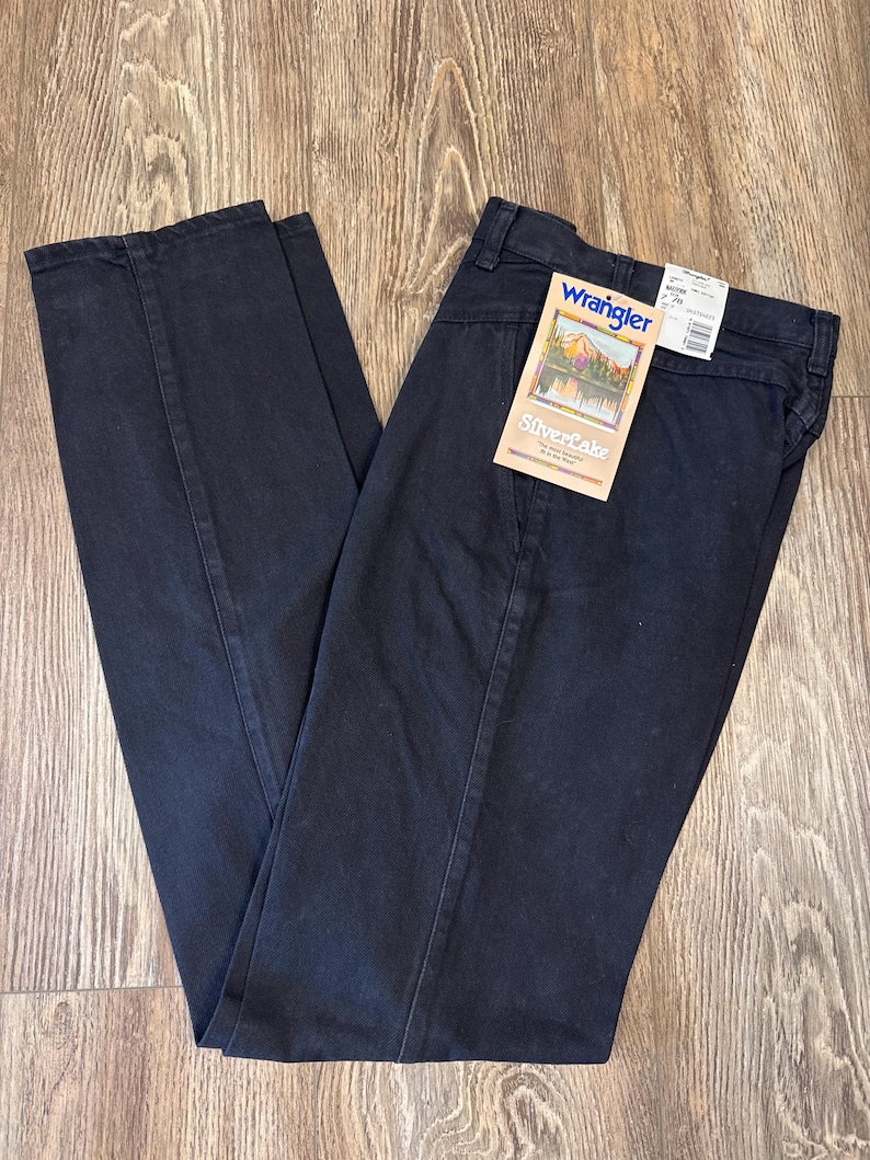 K&ouml;nnte beinhalten: Schwarze gerade Jeans mit einem angebrachten Wrangler Silverlake-Etikett. Das Etikett zeigt eine Bergszene und den Text "Silverlake" in wei&szlig;er Schrift.