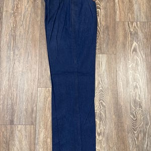 Puede incluir: Un par de pantalones vaqueros de color azul oscuro con ribete de cuero marr&oacute;n alrededor de los bolsillos y la cintura.