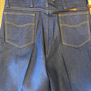 Peut inclure: Un jean en denim bleu fonc&eacute; avec deux poches arri&egrave;re et des d&eacute;tails de couture jaunes.