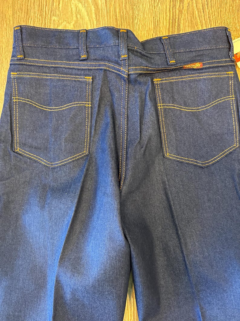 Peut inclure: Un jean en denim bleu fonc&eacute; avec deux poches arri&egrave;re et des d&eacute;tails de couture jaunes.