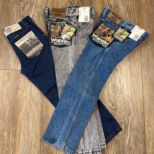 Puede incluir: Tres pares de pantalones vaqueros de mezclilla azul, un par es un lavado azul oscuro, un par es un lavado azul claro y un par es un lavado gris claro con un patr&oacute;n moteado. Los tres pares tienen una etiqueta Wrangler y las palabras "Rugged Wear" en la etiqueta.