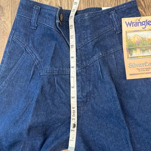 Puede incluir: Pantalones vaqueros azul oscuro con cintura alta y cierre de bot&oacute;n. Una cinta m&eacute;trica muestra una longitud de aproximadamente 33 cm. Los pantalones tienen una etiqueta que dice "Wrangler Silverlake".