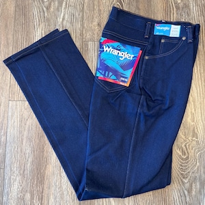 K&ouml;nnte beinhalten: Dunkelblaue Jeans aus Denim mit einem Wrangler-Etikett auf der Ges&auml;&szlig;tasche. Das Etikett zeigt das Wrangler-Logo und den Text "Stone Wash".