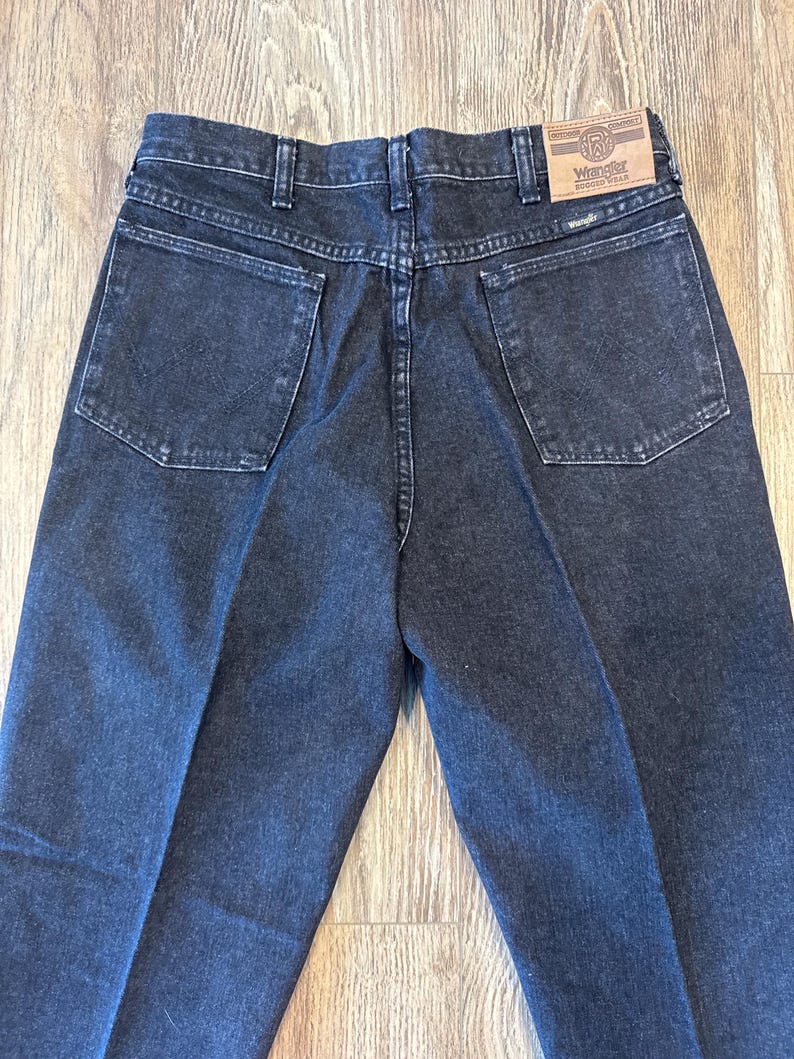 Puede incluir: Un par de pantalones vaqueros de color negro con una etiqueta de Wrangler de cuero marr&oacute;n en el bolsillo trasero.