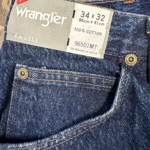 May include: Close-up of dark blue Wrangler jeans. The label indicates a size of 34 x 32 inches (86cm x 81cm) and states the jeans are 100% cotton. The tag also says "Made in U.S.A."