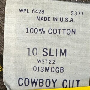 May include: Close-up of a tag from a pair of jeans. The tag reads "WPL 6428", "MADE IN U.S.A.", "100% COTTON", "10 SLIM", and "COWBOY CUT". The tag is white with black text.