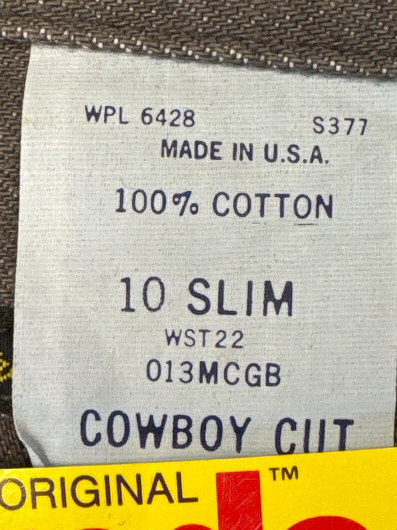 May include: Close-up of a tag from a pair of jeans. The tag reads "WPL 6428", "MADE IN U.S.A.", "100% COTTON", "10 SLIM", and "COWBOY CUT". The tag is white with black text.