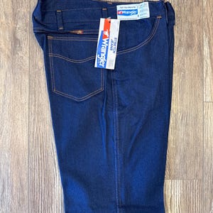 Peut inclure: Un jean en denim bleu fonc&eacute; avec une &eacute;tiquette Wrangler. L'&eacute;tiquette indique "Stretch Jeans" et "Full 1 Year Warranty".