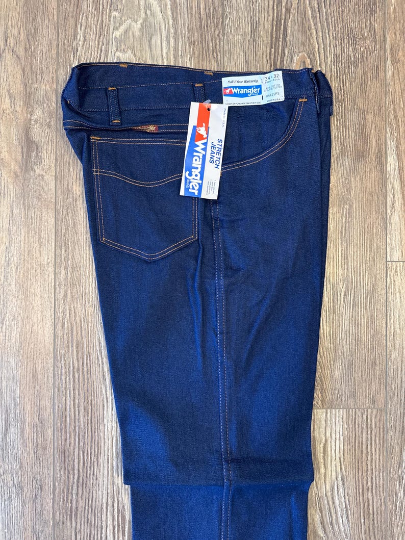 Peut inclure: Un jean en denim bleu fonc&eacute; avec une &eacute;tiquette Wrangler. L'&eacute;tiquette indique "Stretch Jeans" et "Full 1 Year Warranty".