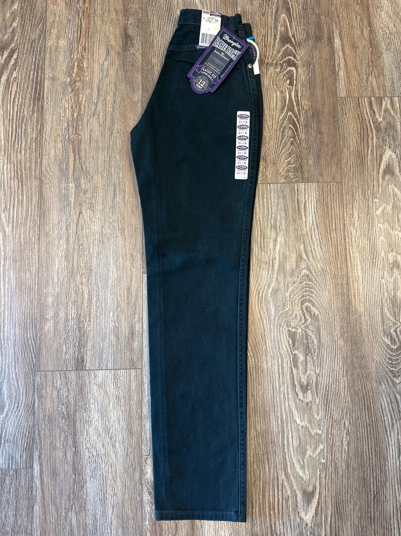 May include: Dark green denim jeans with a Wrangler label and a size 12 tag. The jeans have a classic fit.