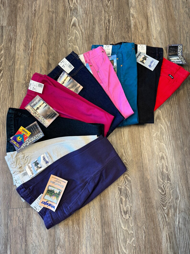 May include: A stack of ten pairs of blue, red, pink, white and beige jeans with the Wrangler Silver Jeans label.
