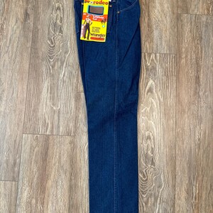 May include: A pair of dark blue denim jeans with a Wrangler label and a yellow and red tag that says "Rodeo Cowboy Cut".