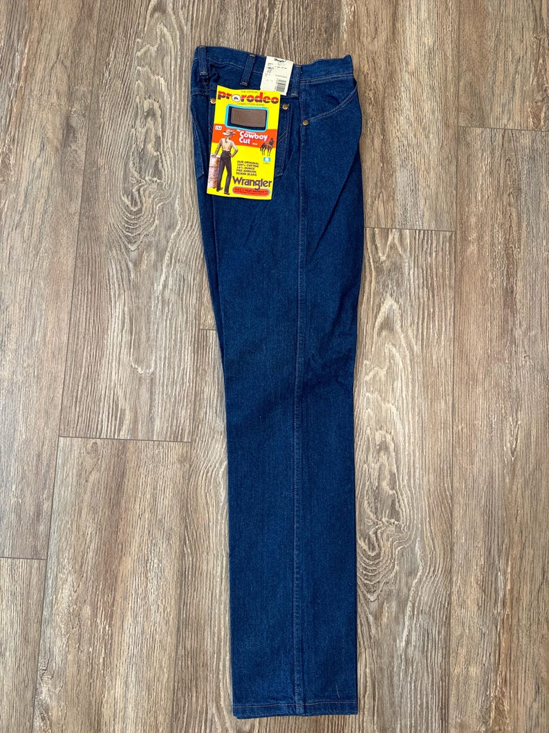 May include: A pair of dark blue denim jeans with a Wrangler label and a yellow and red tag that says "Rodeo Cowboy Cut".
