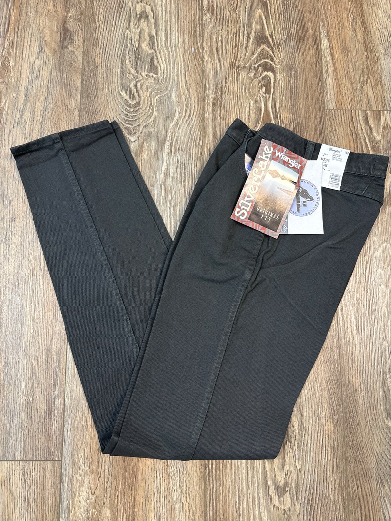 Op de afbeelding: Zwarte denim jeans met een Wrangler Silverlake Original Fit-label eraan bevestigd. Het label toont een panoramisch beeld van een meer en bergen.