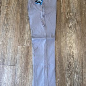 May include: Light blue denim pants with a straight leg. The pants have a classic five-pocket design and a Wrangler tag attached. The pants are laid flat on a wooden surface.