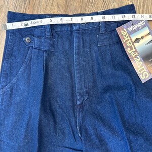 Puede incluir: Primer plano de pantalones vaqueros azul oscuro con cierre de bot&oacute;n y pliegues. Una cinta m&eacute;trica muestra una medida de cintura de aproximadamente 35.5 cm. Una etiqueta Wrangler Silverlake est&aacute; adjunta.